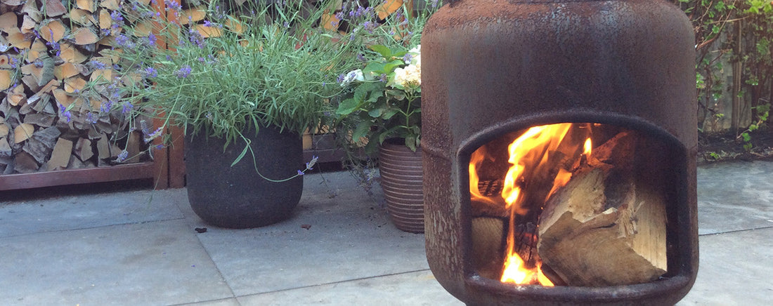 Een sfeervolle buitenruimte met een knisperend vuur: een houtkachel of vierkante cortenstaal vuurschaal zorgt voor warmte en gezelligheid in de tuin, het hele jaar door.