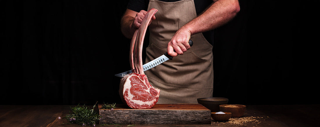 Maatwerk buitenkeuken met geïntegreerde The Bastard kamado, sfeervolle LED-verlichting, spoelbak, koelkast en luxe afwerking in een stijlvolle tuinomgeving.