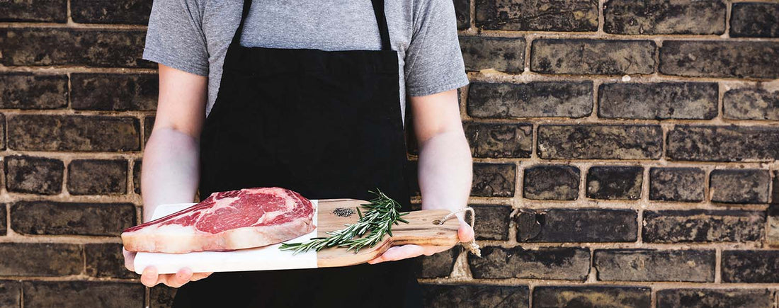Een kamado-barbecue van The Bastard in een stijlvolle buitenkeuken, omringd door accessoires zoals een pizzasteen, gietijzeren rooster en Dutch oven.